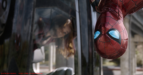 Spider-Man hangs upside down next to a dark window reflecting a woman's face.