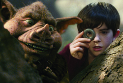 A young boy holding a small ring up to his eye next to a large, brown, pig-like creature.