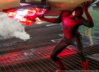 Spider-Man in a red and black suit lifting a large, glowing object above his head.
