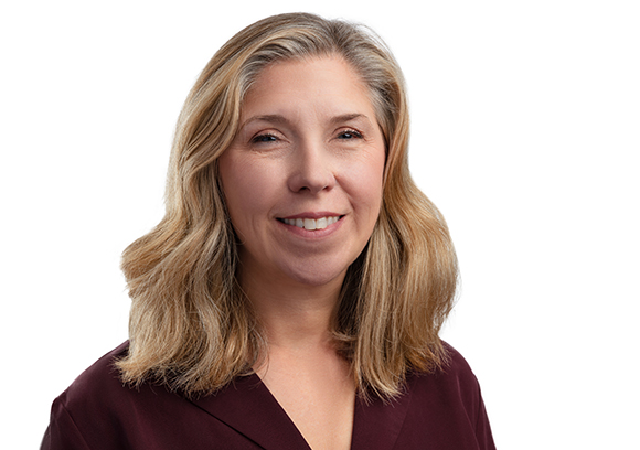 A smiling woman with shoulder-length blonde hair wearing a maroon top against a white background.