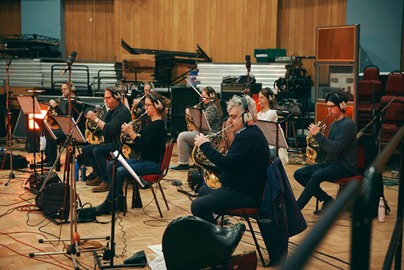 Musicians in a studio playing French horns and other brass instruments while wearing headphones.