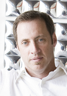 A man with short brown hair and a small goatee wearing a white collared shirt.