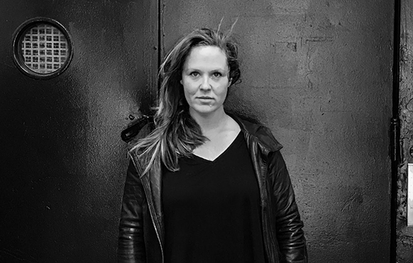 Black and white portrait of a woman with long hair wearing a leather jacket and black shirt.