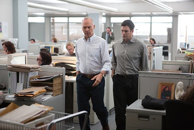 Two men in button-down shirts walk through a busy office filled with cubicles and paperwork.