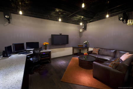 A lounge area with a brown leather sectional, an orange rug, a coffee table, and a desk with computer monitors.