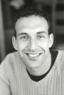 Black and white headshot of a smiling man wearing a light-colored sweater.