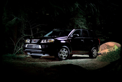 A dark SUV parked on a dirt path in a dark forest at night.
