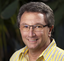 A smiling man with short brown hair and glasses wearing a yellow striped shirt.