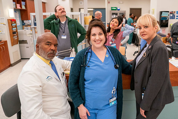 A group of diverse medical professionals, including doctors and nurses, posing in a hospital hallway.