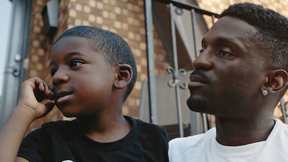 A young boy and a man sit side-by-side, looking thoughtfully toward the left.