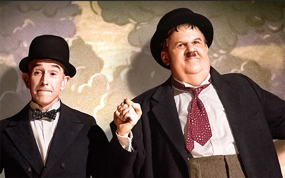 Two men in bowler hats, suits, and ties posing against a cloudy background.