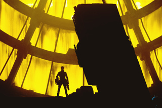 Silhouette of a person standing in front of a large, curved, glowing yellow architectural structure.