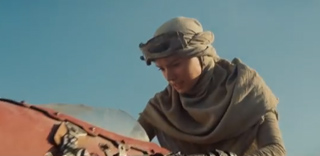 A person wearing a tan headwrap and goggles leans over a red piece of equipment under a clear blue sky.