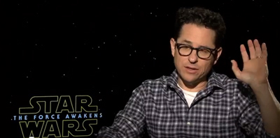 A man with glasses and a plaid shirt gestures with one hand against a starry Star Wars background.