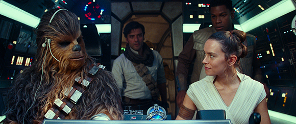 A Wookiee, a woman in white, and two men stand inside a dimly lit, high-tech spaceship cockpit.