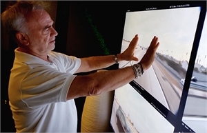 A man in a white polo shirt reaches toward a large digital display showing a highway view.