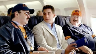Three men sit in airplane seats, including one in a tan blazer and two in sports apparel.