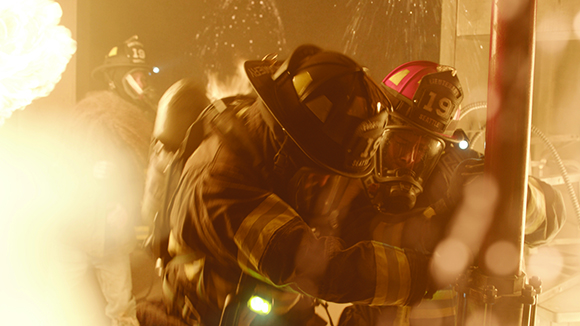 Firefighters in protective gear and helmets working amidst smoke and bright light.