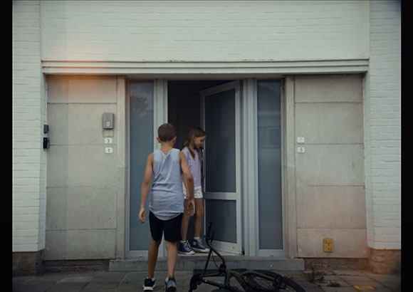 A boy in a grey tank top and a girl in a purple shirt stand in a building entrance.