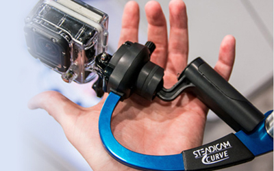 A person holds a small action camera attached to a black and blue handheld stabilizer.