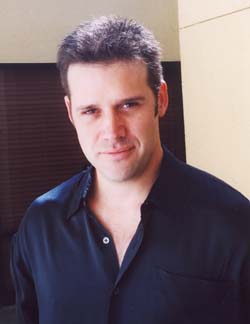 A man with short dark hair wearing a dark navy button-down shirt looking forward.