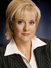 A blonde woman wearing a white collared shirt and a dark pinstripe blazer looks toward the camera.