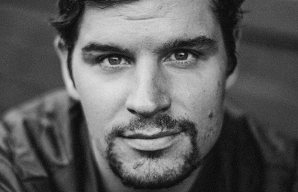 Black and white close-up portrait of a man with dark hair and a goatee looking directly at the camera.