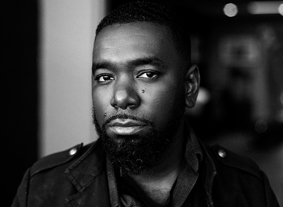 Black and white close-up portrait of a man with a beard and short hair looking toward the camera.