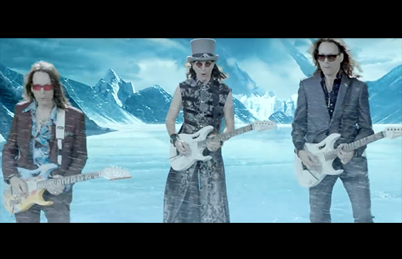 Three musicians playing white electric guitars in a snowy, mountainous landscape.