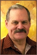 A middle-aged man with short graying hair and a dark mustache smiling against a gold background.