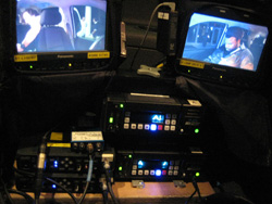 Several small video monitors displaying footage above stacked electronic control units and wiring.