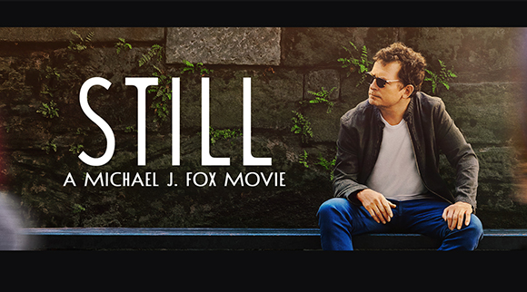 A man in sunglasses and a dark jacket sits against a stone wall with the title STILL in large white letters.