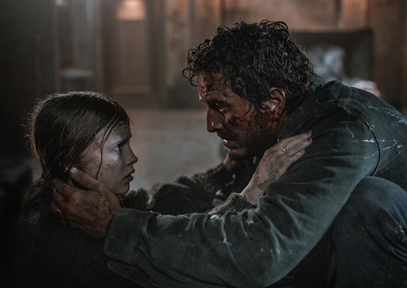 A man with dark curly hair and a young girl look at each other with dirt and blood on their faces.