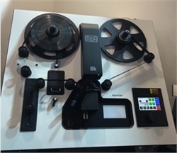 A black reel-to-reel tape recorder with two large reels and a control panel on a white tabletop.