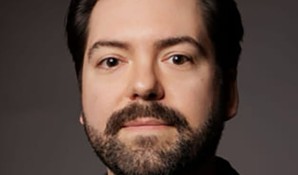 Close-up portrait of a man with dark hair and a groomed beard looking directly at the camera.