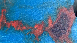 Red and dark purple pigment spreads across a textured blue surface.