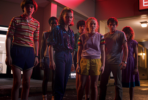 A group of seven teenagers standing in a line outdoors at night under red lighting.
