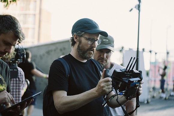 A man wearing a black t-shirt and cap holds a professional camera rig outdoors.