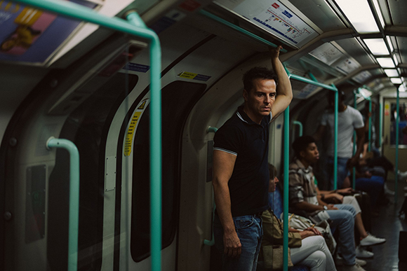 A man in a dark polo shirt stands in a subway car, holding an overhead rail.