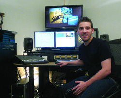 A man sits at a desk equipped with multiple monitors, speakers, and an audio mixing console.