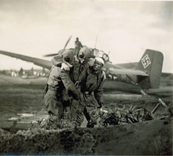 Group of soldiers in uniform embracing in a field before a propeller plane with a swastika on the tail.