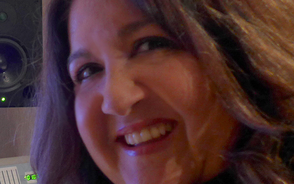 A close-up portrait of a smiling woman with dark, wavy hair.