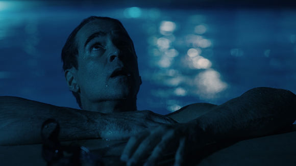 A man looks upward with a startled expression while his head and arms emerge from dark blue water.