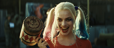 A woman with blonde and blue pigtails smiles widely while holding a large, decorated mallet.