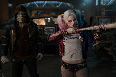 A woman with blonde and pink pigtails holds a baseball bat next to a large, hooded man in a dark warehouse.