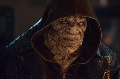 Close-up of a person with textured, scaly reptilian skin wearing a dark brown hooded jacket.