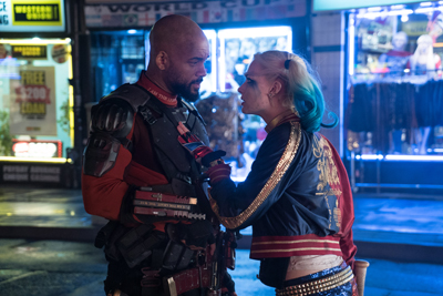 A man in tactical armor and a woman with blue hair stand face-to-face in a nighttime city setting.