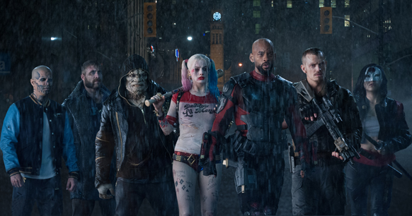 Six costumed characters stand in a line on a dark, rainy city street at night.