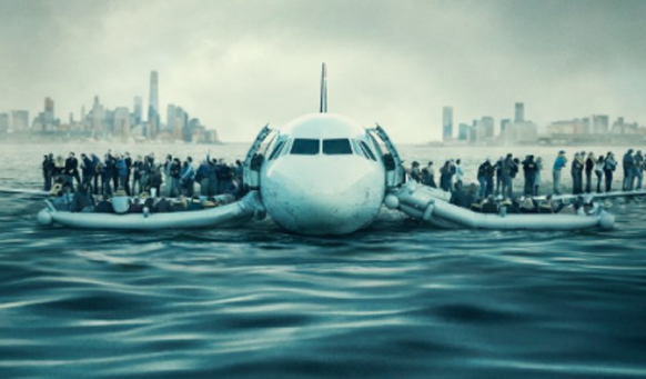 A large passenger plane floats on choppy water with crowds of people standing on its wings near a city skyline.