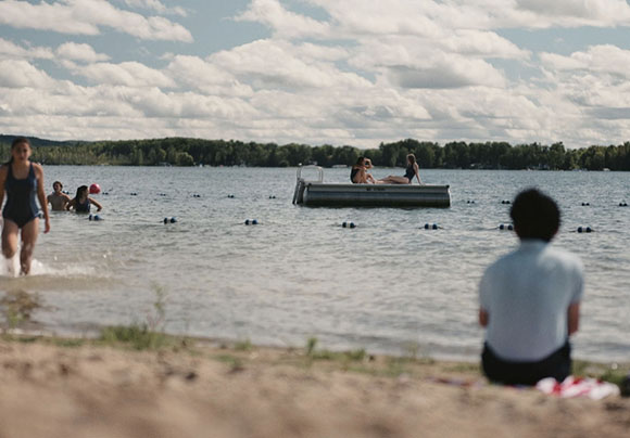 People swimming and lounging on a raft in a large lake under a cloudy sky.